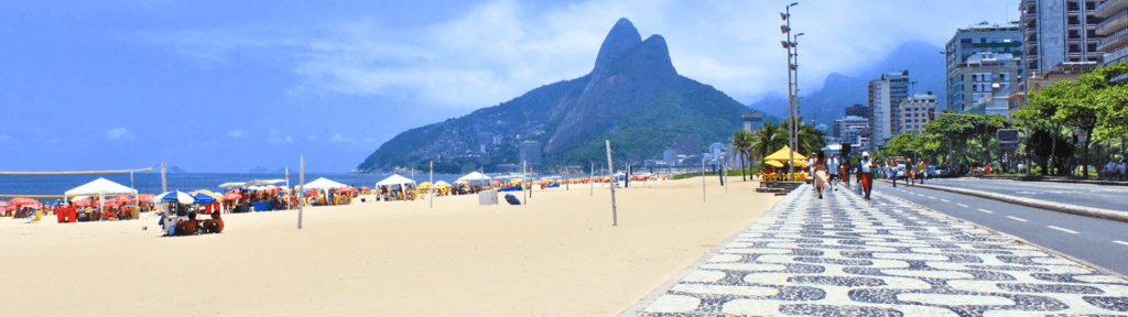 Ipanema: sofisticação, estilo de vida e hospedagem premium no Rio Orla de Ipanema em dia ensolarado, com calçadão, praia ampla, montanhas ao fundo e turistas caminhando, representando uma experiência premium e valorizada no aluguel por temporada.
