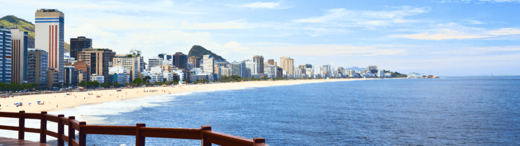 Leblon: exclusividade, tranquilidade e alto padrão de hospedagem Vista da Praia do Leblon com mar calmo, prédios residenciais de alto padrão e ambiente mais tranquilo, simbolizando exclusividade e estadias longas e qualificadas no Rio de Janeiro.