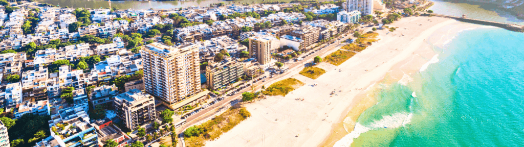 Barra da Tijuca: conforto, espaço e imóveis ideais para estadias prolongadas Vista aérea da Barra da Tijuca com praia extensa, condomínios modernos e mar azul, destacando imóveis amplos, infraestrutura moderna e perfil ideal para estadias longas.