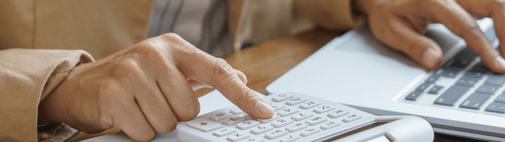 Mãos usando calculadora ao lado de um notebook, simbolizando o tempo gasto com tarefas operacionais e decisões financeiras no aluguel por temporada.