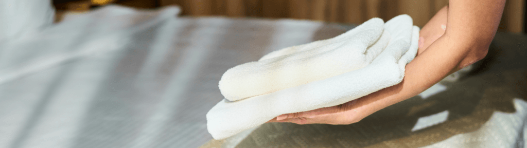 Toalhas brancas sendo organizadas sobre a cama representando operação e padronização no aluguel por temporada